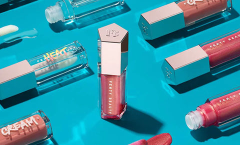 Editorial shot of one Gloss Bomb Universal Lip Luminizer standing up and various lip glosses laying down around.