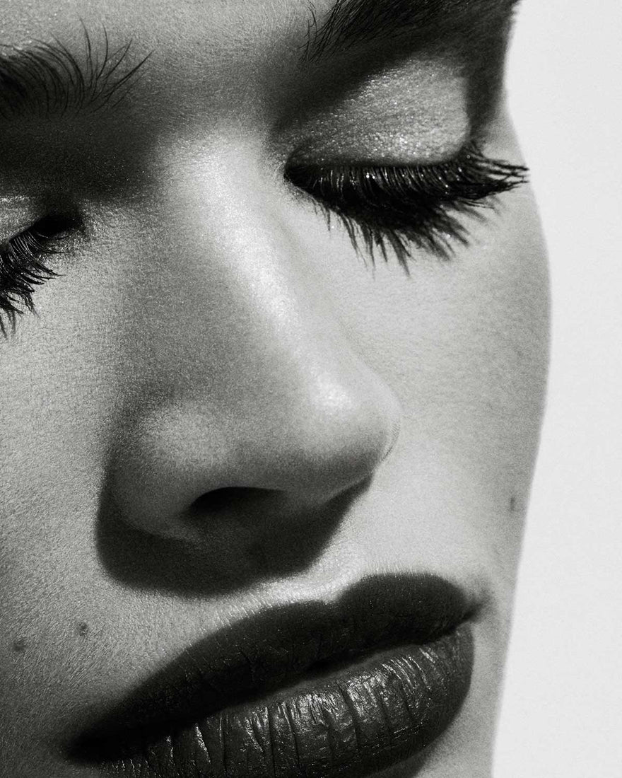  Black and white image of a model's face with closed eyes, elegantly showcasing the impact of Full Frontal Volume, Lift & Curl Mascara on her lashes.