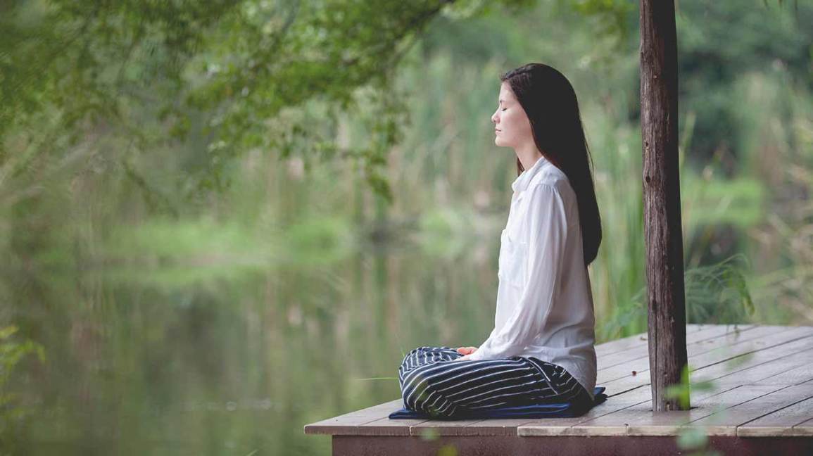 woman meditating on a pier on a small lake