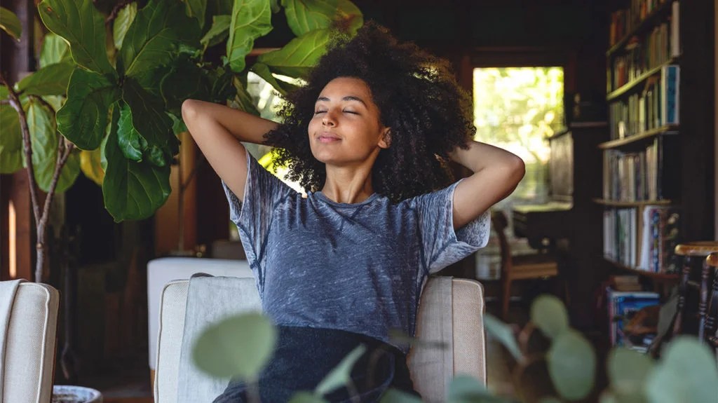 A female sitting on an arm chair, stretching, and relaxing with her eyes closed.