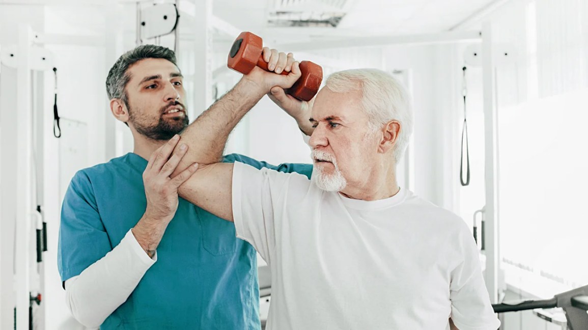 A physical therapist helps a patient to do a physical therapy exercise using a handheld weight. 