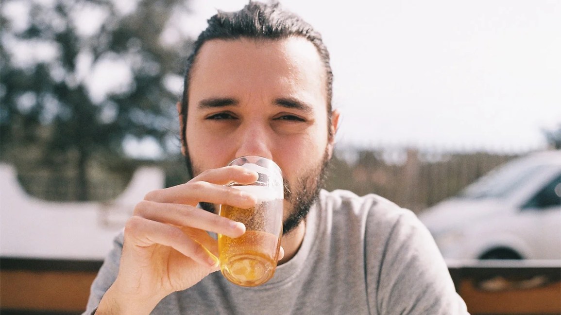 A man sips an alcoholic drink at an outdoor bar. 