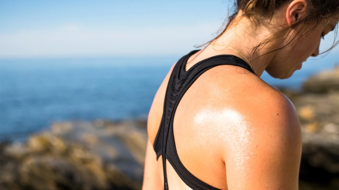 A woman in workout gear stands sideways with sweat on her back. 