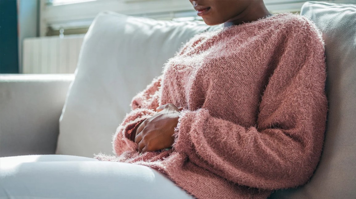 A woman sits on a couch, holding her stomach. 