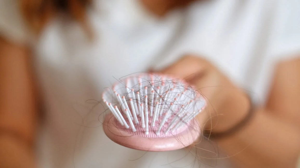 pink hairbrush filled with long strands of hair between the bristles