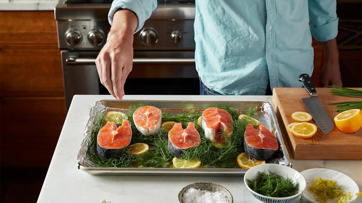 man sprinkling spices on raw salmon in baking tray