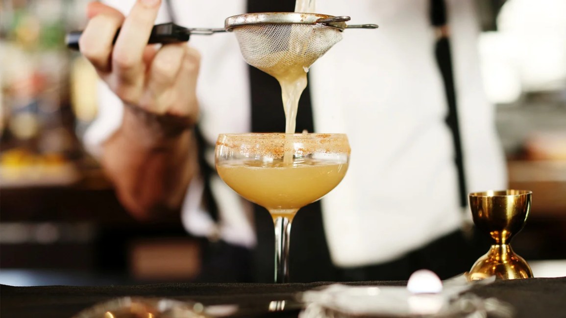 hand holding small strainer above a full cocktail glass