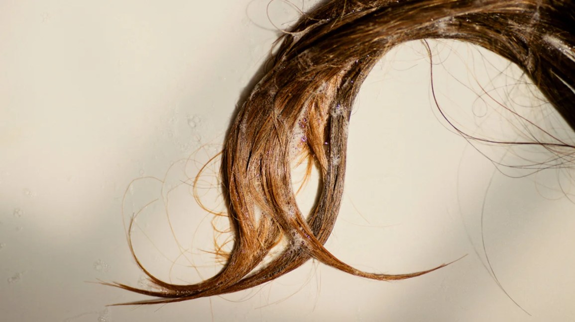 Strands of wet, soapy hair curling on plain background