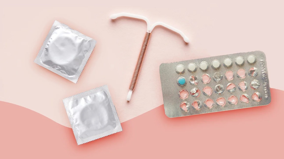 condoms, birth control pills, and iud on pink backdrop