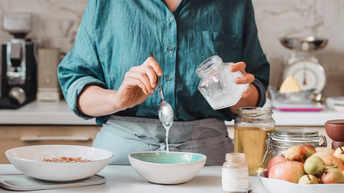 Person standing at a kitchen counter spooning coconut oil into a bowl