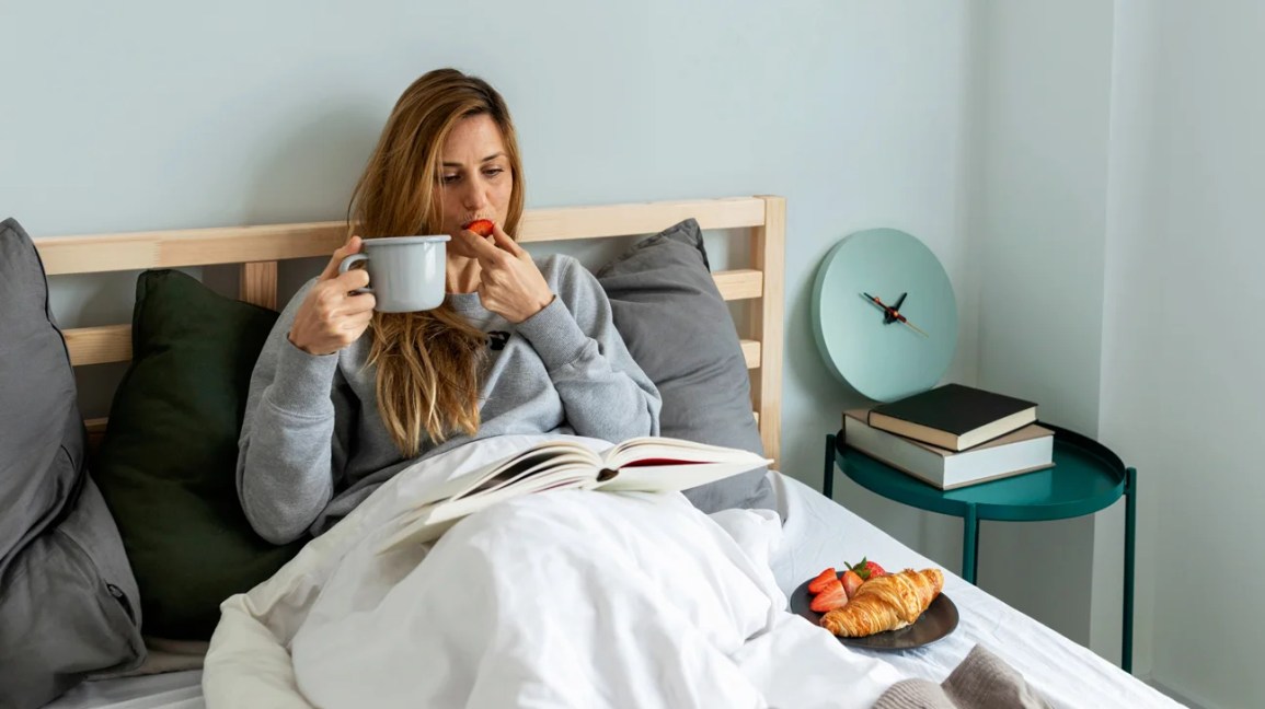 woman in bed eating breakfast with coffee and book