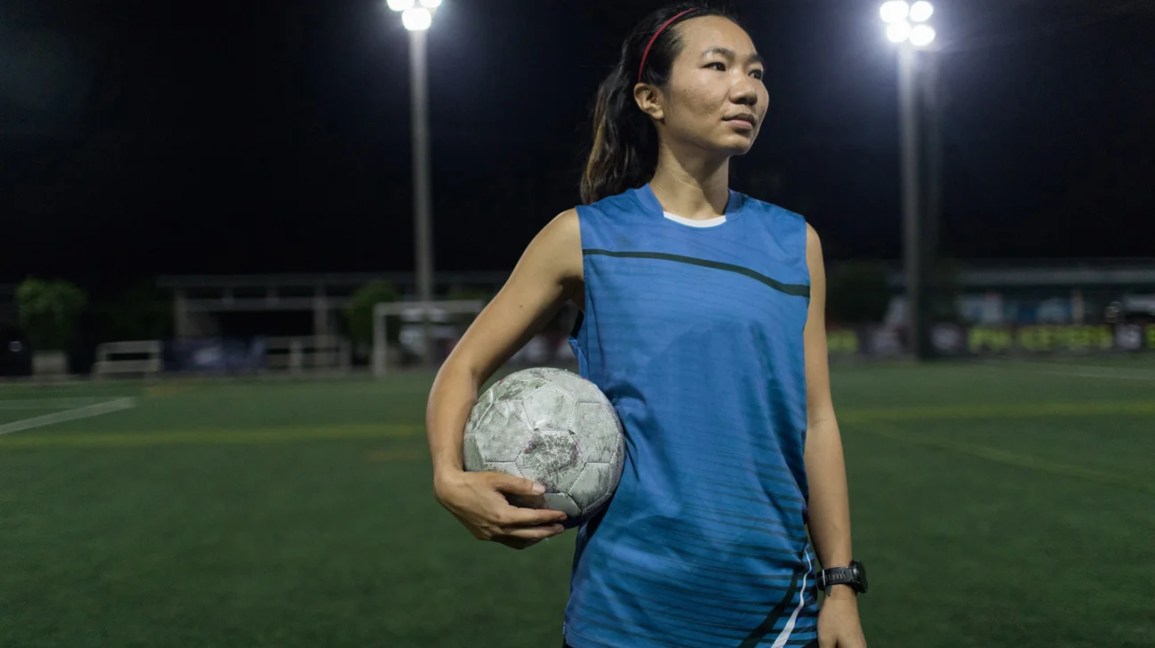 woman standing on soccer field holding soccer ball to hip