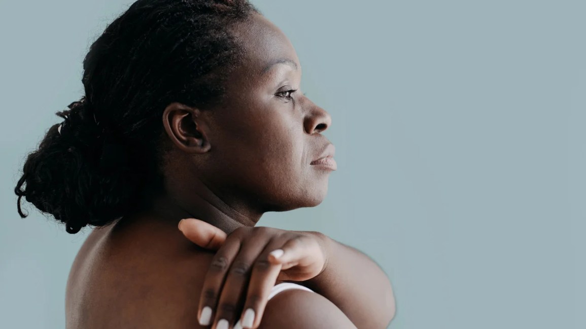 Black woman performing skin care routine with arm reaching over shoulder to her upper back