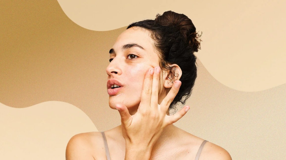 person with dry skin applies skin care product against wavy beige background