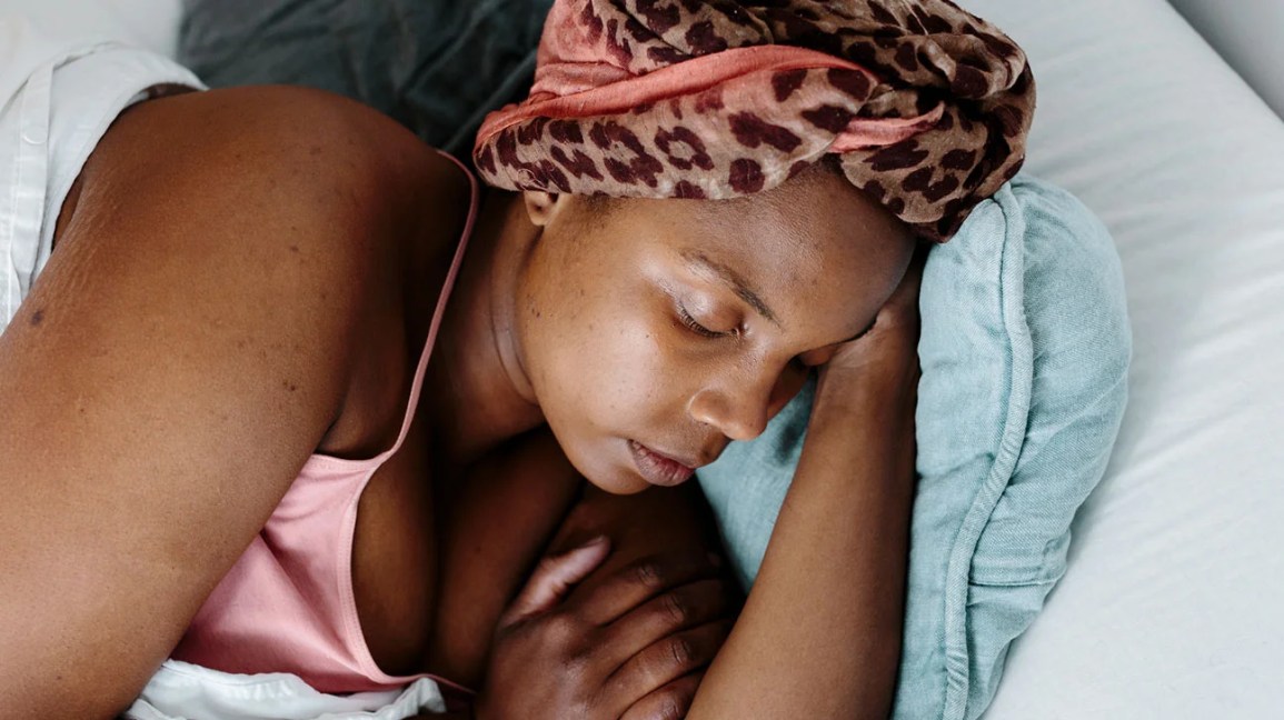 Woman in pink tank top sleeping in bed with hair wrapped up