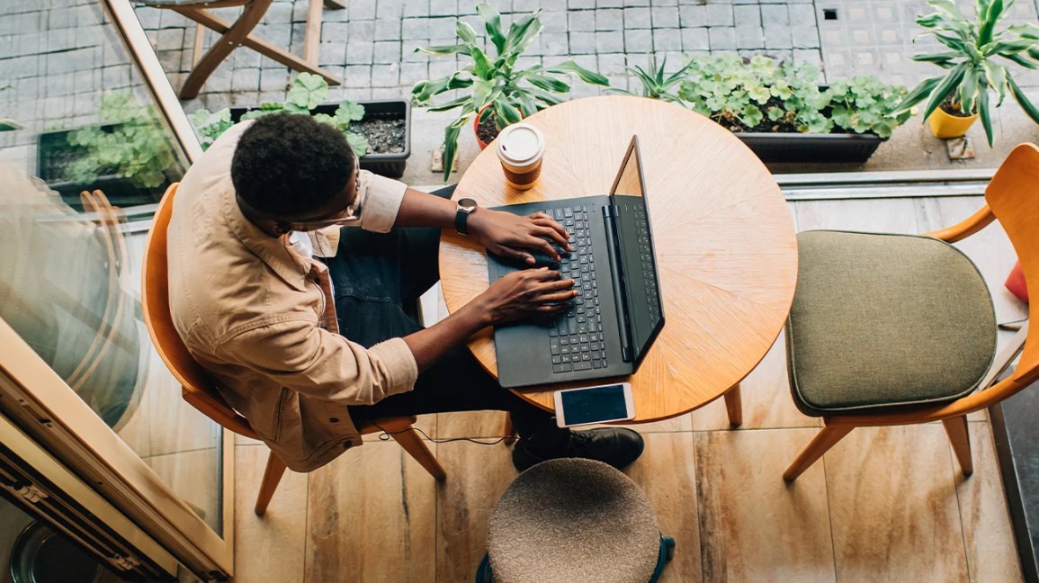 Person wearing glasses sitting at round table typing on laptop