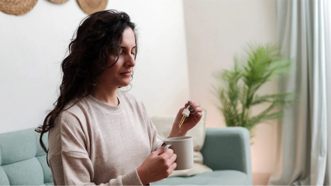 A woman puts vitamin D drops into a cup of tea