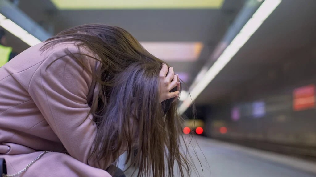 A woman holding her head in her hands on a train platform during an episode of psychosis.