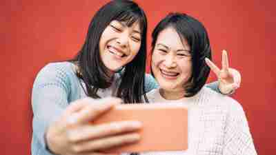 Asian mother and daughter taking photo selfie with mobile smartphone outdoor - Happy Chinese family having fun with new trends technology apps - Family, tech and lifestyle people concept