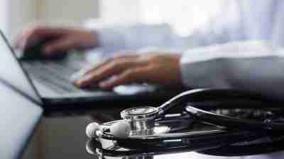 Female doctor in white lab coat typing on laptop computer with notebook and medical stethoscope on the desk at workplace. Medical technology ,Electronic health record system (EMR) concept