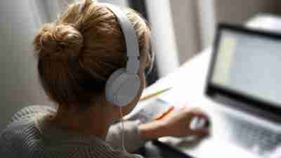 Blonde woman with headphones working on notebook computer.