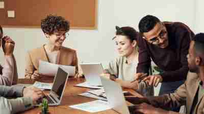 Coworkers gathered around a table engaged in conversation. A positive work environment helps all employees, including neurodivergent employees, thrive.