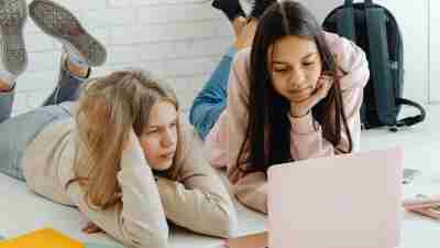 Two teenage girls laying down while on their laptop. Autism in girls is often overlooked.