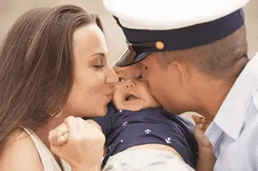 Man with military cap and Women embracing and kissing small child in military style clothing 