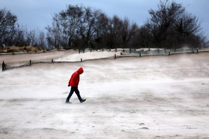 Wetter zu Silvester: Ein Mann geht im Sturm am Ostseestrand entlang, der vom Wind verwehte Sand leuchtet hell in Warnemünde, am 21. Dezember 2023