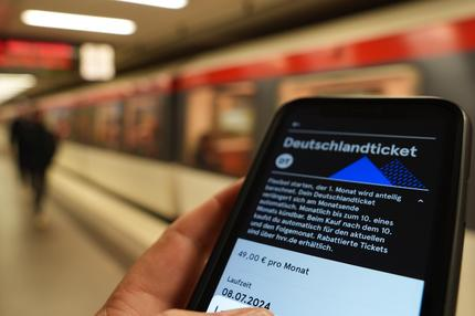 Nahverkehr: Ein Fahrgast hält ein Smartphone mit einem digitalen Deutschlandticket an einer U-Bahnstation in der Hand.