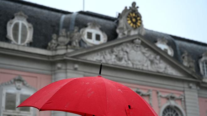 Launisches Wetter in NRW: Eine Frau geht mit ihrem Regenschirm bei Regen am Schloss Benrath vorbei.