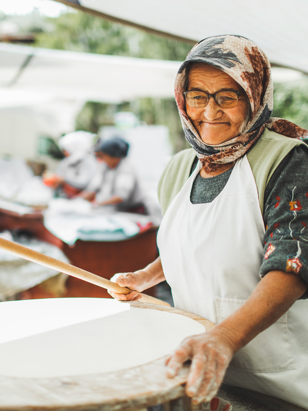 Türkische Gözleme: Still life of sliced turkish filo gozleme on chopping board

Muslim cuisine and culture. Street food on local rustic market. Eastern appearance and modest clothing of senior woman. Working with pleasure.