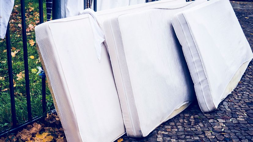 Three mattresses leaning on a fence in the street.