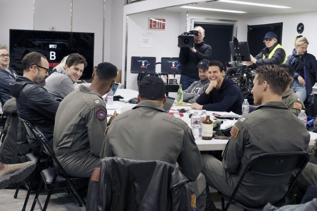 2J8WWE2 TOP GUN: MAVERICK, (aka TOP GUN 2), director Joseph Kosinski (left, gray sweatshirt), Jay Ellis (left of center), Tom Cruise (hand on chin), Glen Powell (front right), on set, 2022. ph: Scott Garfield /? Paramount Pictures / Courtesy Everett Collection