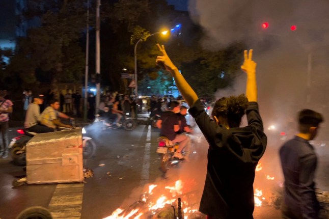 TOPSHOT - A demonstrator raises his arms and makes the victory sign during a protest for Mahsa Amini, a woman who died after being arrested by the Islamic republic's "morality police", in Tehran on September 19, 2022. - Fresh protests broke out on September 19 in Iran over the death of a young woman who had been arrested by the "morality police" that enforces a strict dress code, local media reported. Public anger has grown since authorities on Friday announced the death of Mahsa Amini, 22, in a hospital after three days in a coma, following her arrest by Tehran's morality police during a visit to the capital on September 13. (Photo by AFP) (Photo by -/AFP via Getty Images)