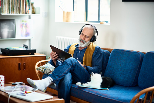 Hipster man wearing headphones listening to record and reading cover