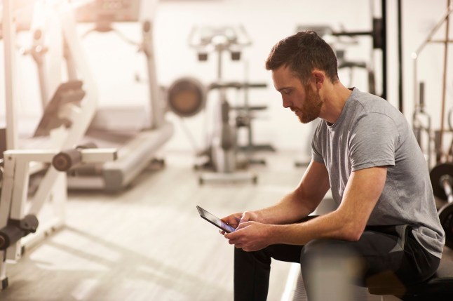 A man sits and uses a digital tablet after a gym workout.