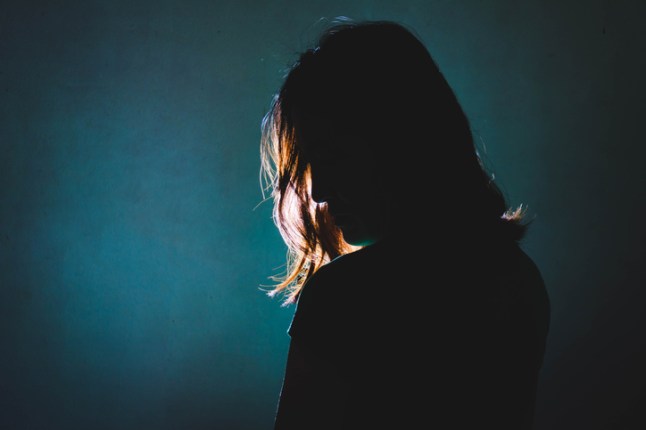 silhouette of depress woman standing in the dark with light shine behind