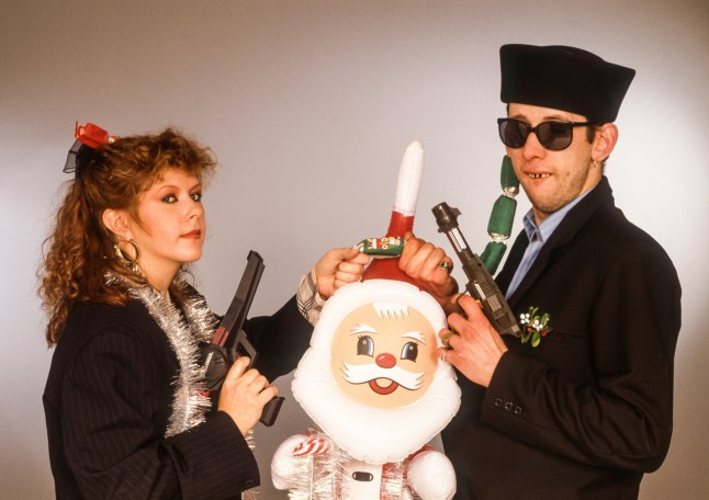 Portrait of British musician Kirsty MacColl (1959 - 2000) and Irish musician Shane MacGowan, the latter of the group the Pogues, as they pose together, each holding a toy gun with one hand and, in the other, a Christmas cracker over an inflatable Santa Claus, 1987. (Photo by Tim Roney/Getty Images)