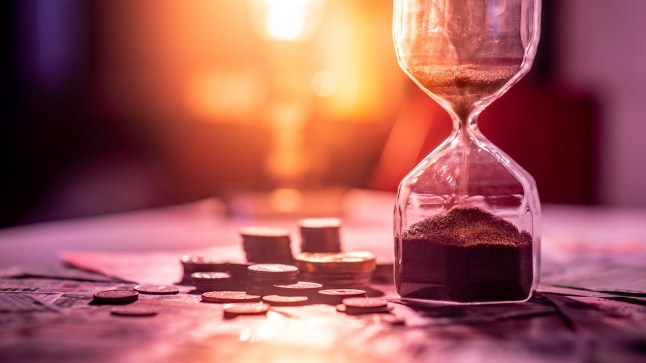 Sand running through the shape of hourglass on table with banknotes and coins of international currency. Time investment and retirement saving. Urgency countdown timer for business deadline concept; Shutterstock ID 1140269075; Purchase Order: -