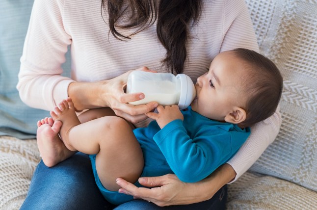 Little infant baby lying on mothers hand drinking milk from bottle. Newborn baby drinking milk from bottle. Cute toddler with milk bottle on leg of mother.