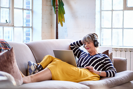 Senior woman wearing headphones watching movie on laptop