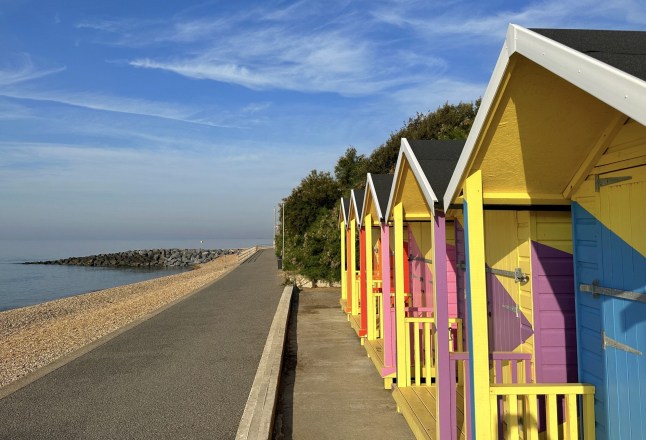 Row of multi coloured wooden beach huts on beach, Folkestone, Kent, England, UK