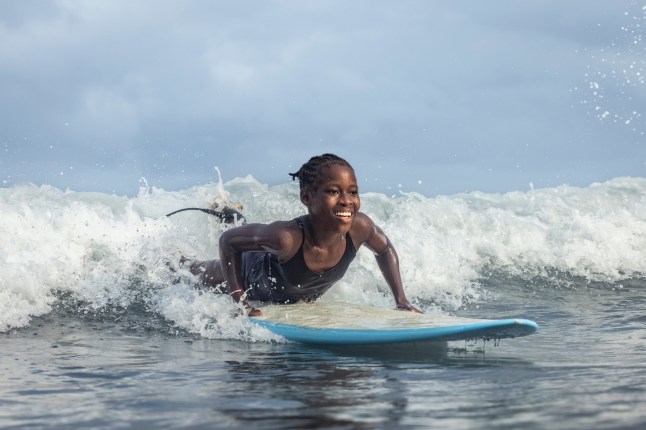 Happy African girl surfer paddling out on surfboard riding a wave with water splashing around her and surfing in Sao Tome and Principe, Africa; Shutterstock ID 2371092469; purchase_order: -; job: -; client: -; other: -