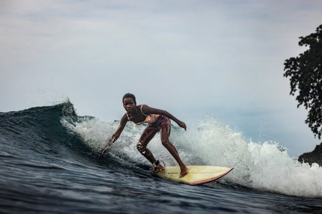 Young black girl surfing a wave and standing on surfboard riding waves in Sao Tome and Principe, Africa; Shutterstock ID 2371092293; purchase_order: -; job: -; client: -; other: -