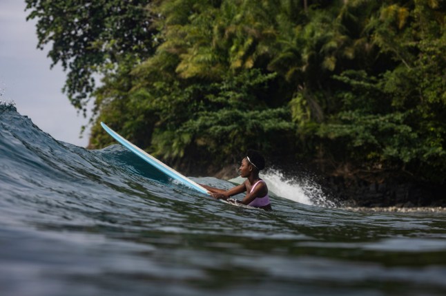 African girl surfer holding onto surfboard riding waves and surfing in Sao Tome and Principe, Africa; Shutterstock ID 2371092507; purchase_order: -; job: -; client: -; other: -