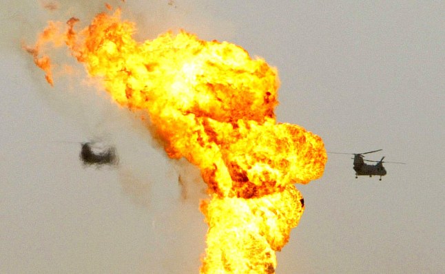 US military helicopters fly past a burning oil well at the Rumayla Oilfields 23 March, 2003 in Iraq. Several oil wells have been set ablaze by retreating Iraqi troops in the Ramaila area, the second largest offshore oilfield in the country, near the Kuwaiti border. AFP PHOTO/POOL/IAN WALDIE (Photo by IAN WALDIE / POOL / AFP) (Photo by IAN WALDIE/POOL/AFP via Getty Images)