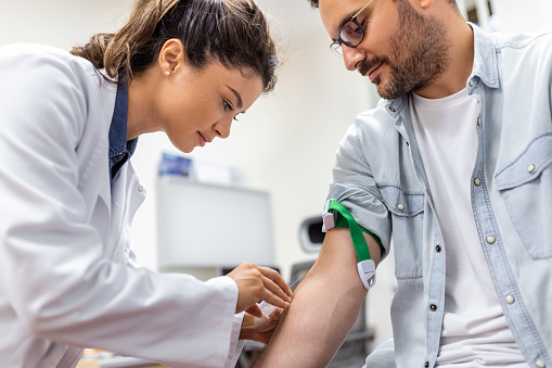 Friendly hospital phlebotomist collecting blood sample from patient in lab. Preparation for blood test by female doctor medical uniform on the table in white bright room