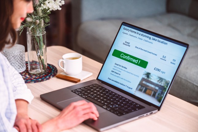 Cheerful Asian woman booking accommodation on travel app on laptop at home