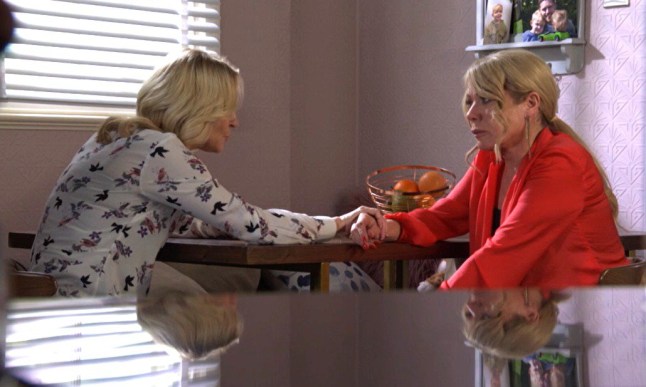 Kathy holding Sharon's hand across the table in EastEnders